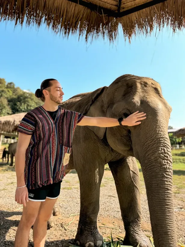 Brent met een hand op de kop van een olifant, onder een rieten dak