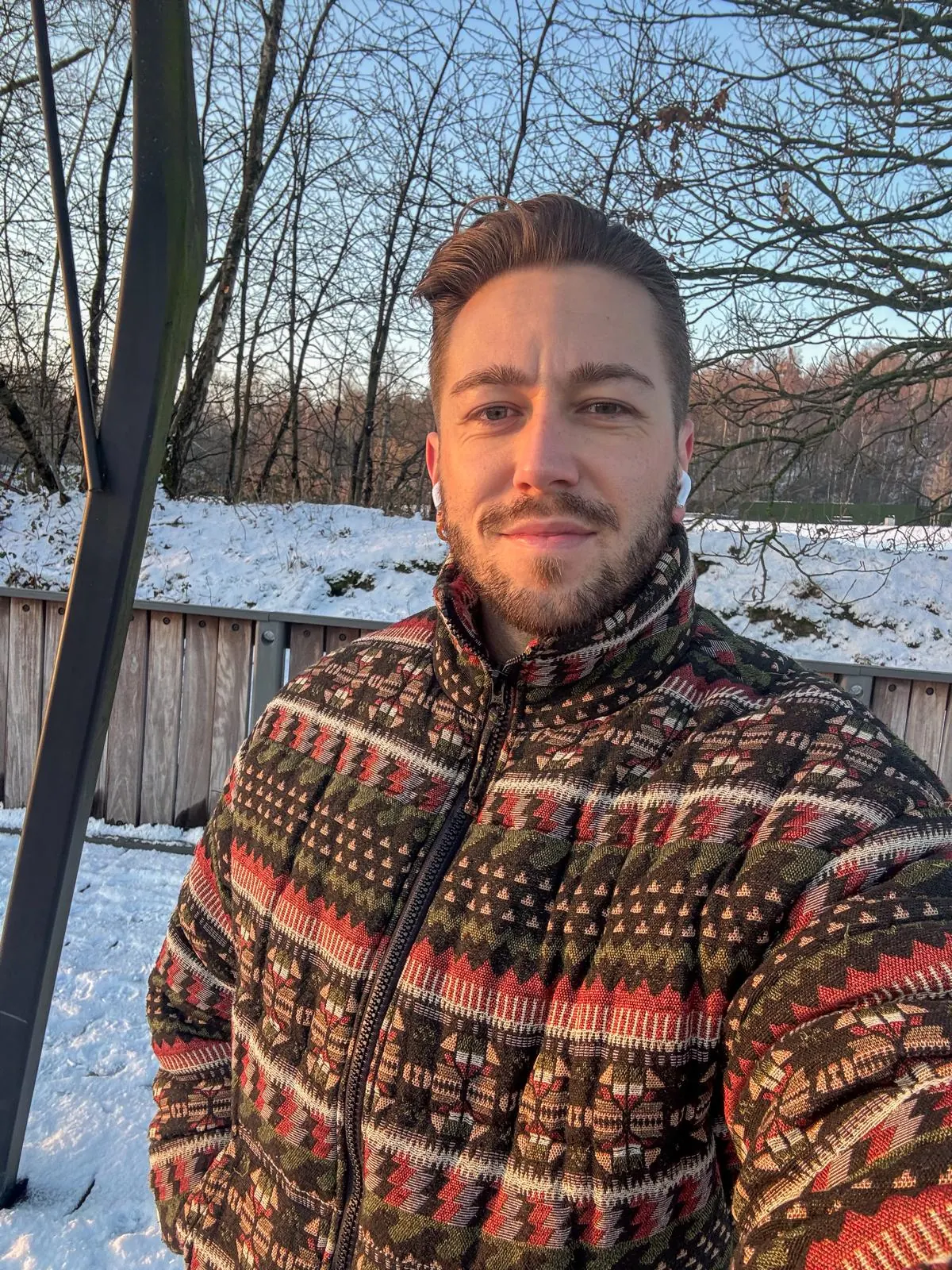 Brent in een gebreide winterjas, met sneeuw en kale bomen achter hem