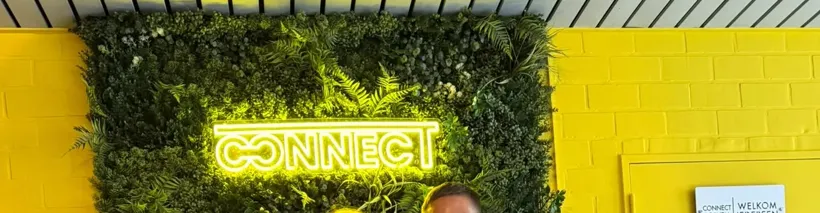 Een lichtgevend CONNECT opschrift in een wand van groen blad, op een gele muur