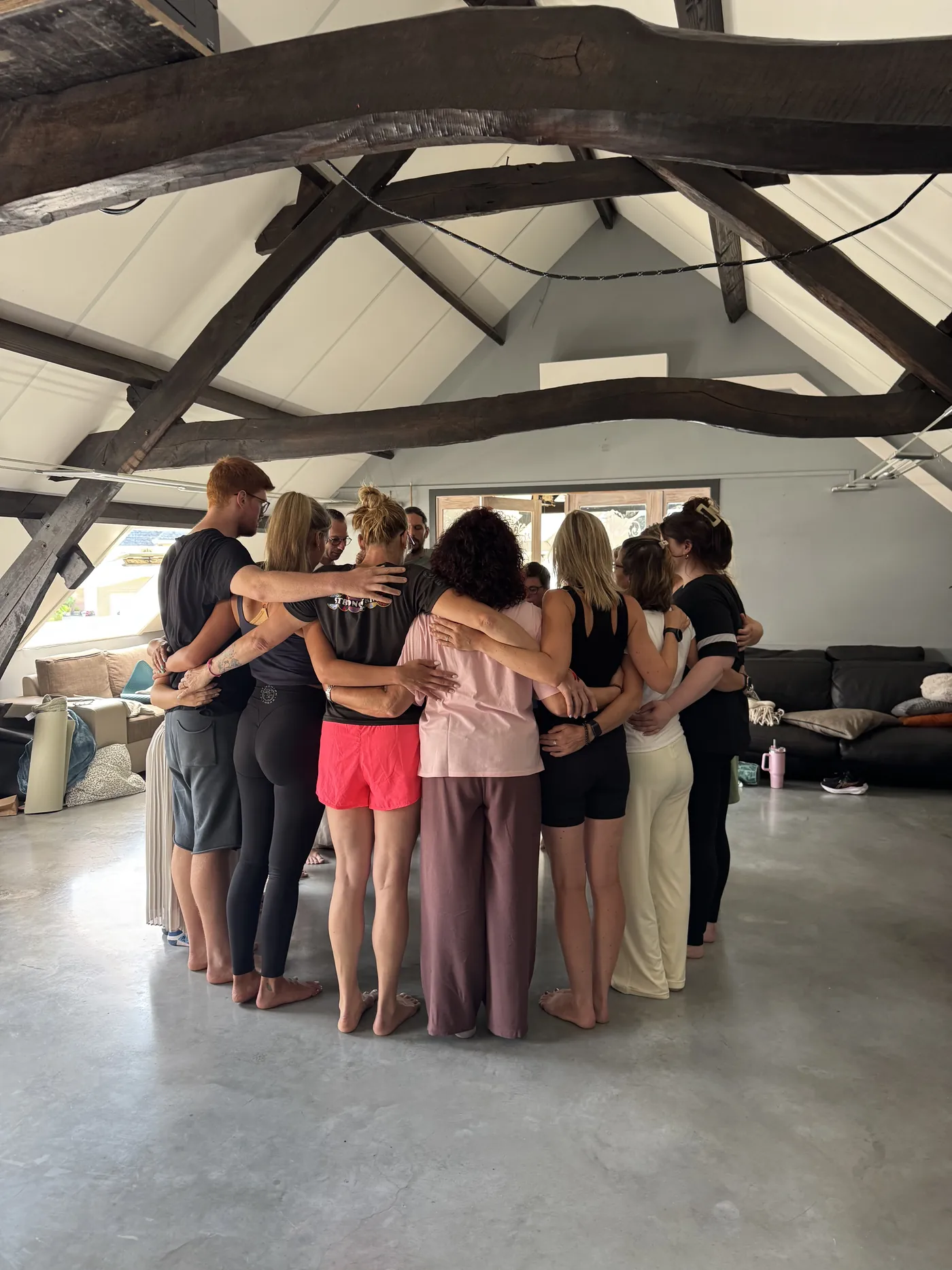 De groep staat in een kring met de armen om elkaar, onder de balken van de retreatruimte