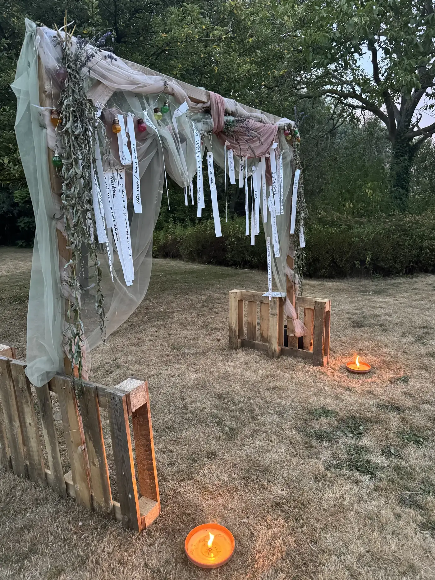 De poort van het retreat in de avond: doeken, briefjes en kaarsen in het gras