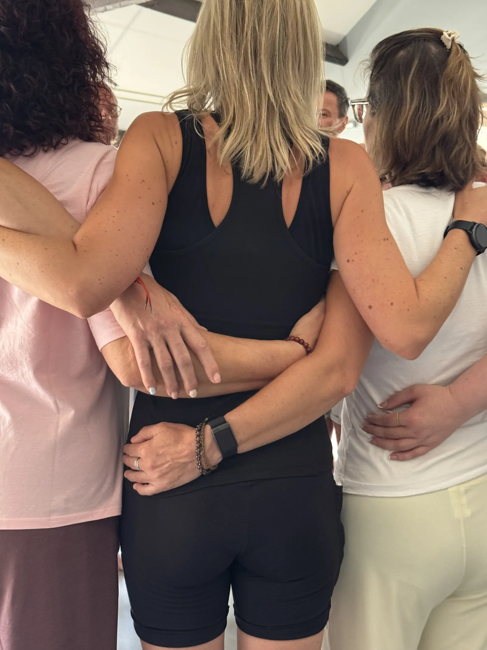 Drie mensen met de armen om elkaar heen, van achteren gezien, tijdens het retreat